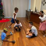 In a room with a wood floor, children play Duck Duck Goose