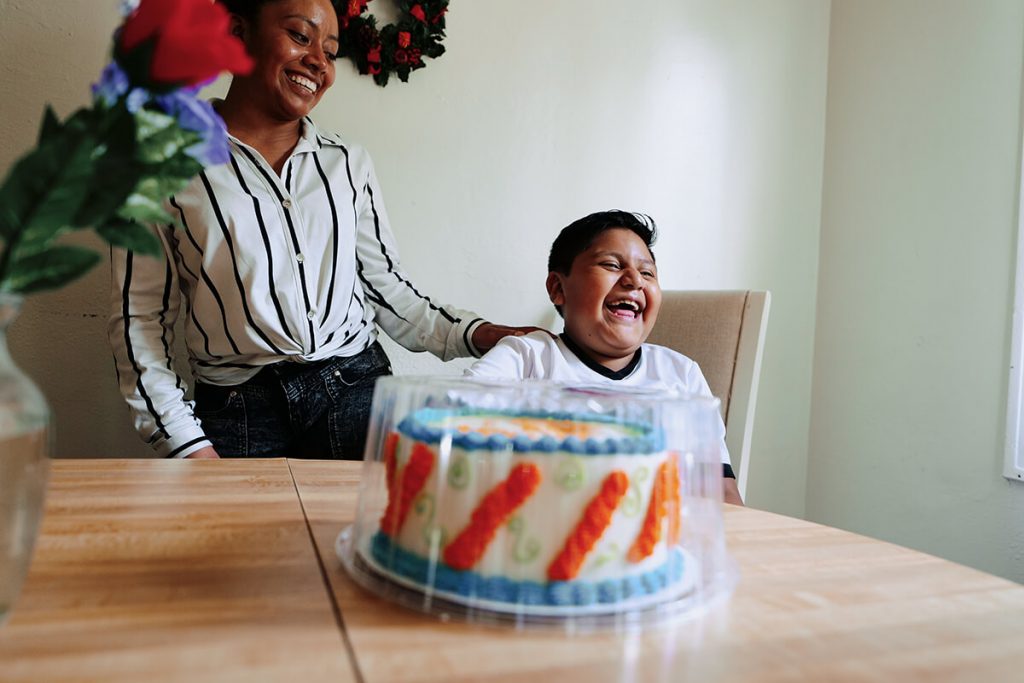 Woman and boy laugh together with cake in foreground