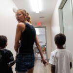 Mom holds hands with her two sons on either side of her as they walk down a hall
