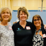 Three women stand in gymnasium made over for luncheon